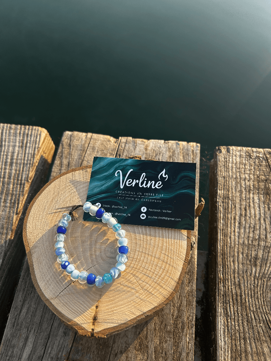 Bracelet en perles de verre bleues et marbrées posé sur une rondelle de bois au bord de l'eau