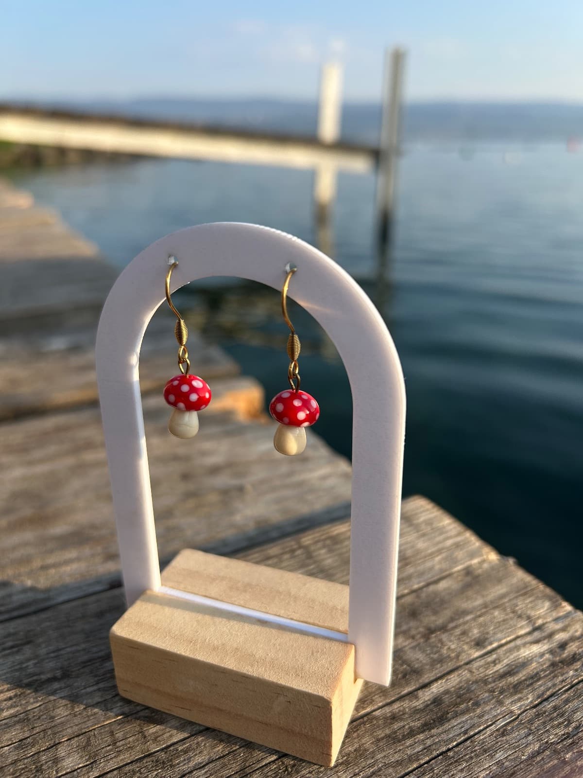 Paire de boucles d'oreilles pendantes aux motifs de champignons rouges à pois blancs sur un présentoir.