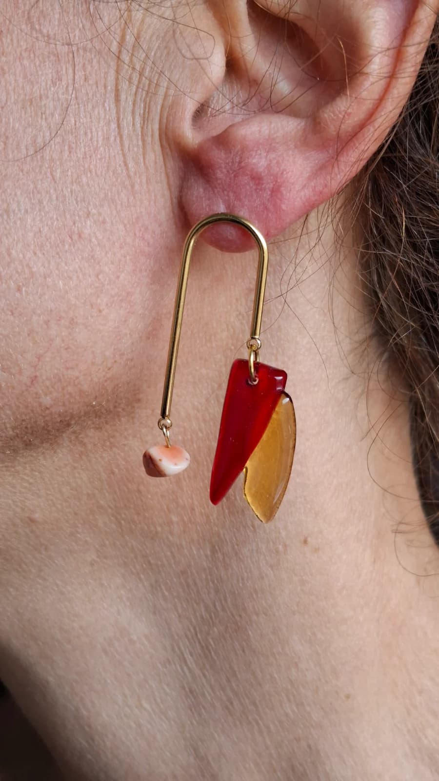 Boucle d'oreille en arche dorée avec pampilles en verre rouge et ambré portée à l'oreille