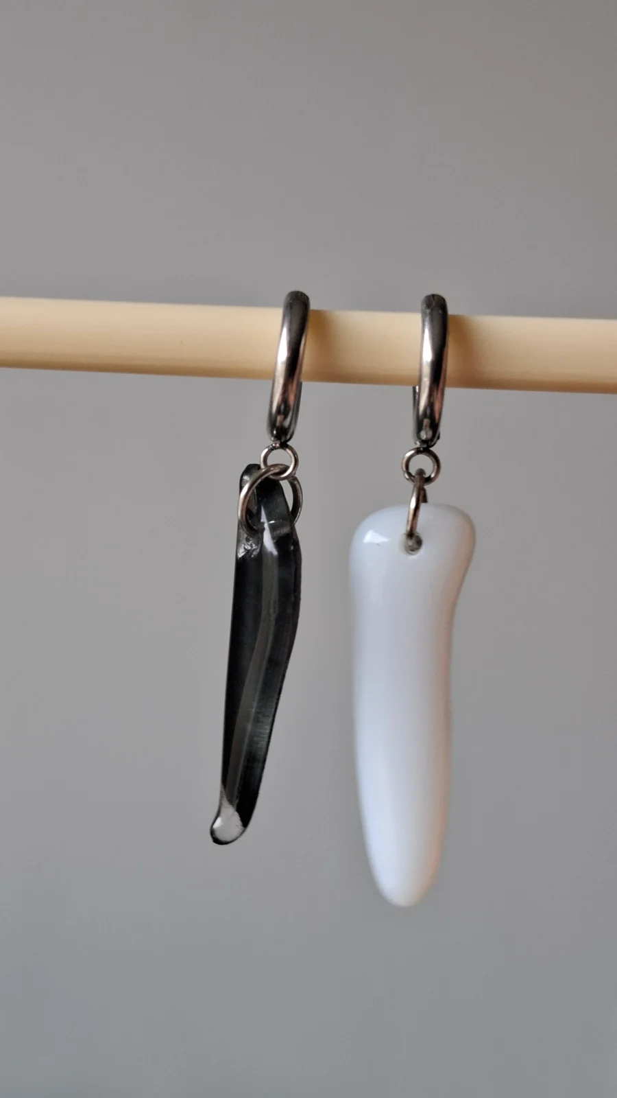 Paire de boucles d’oreilles pendantes, une noire et une blanche, suspendues à une baguette en bois.