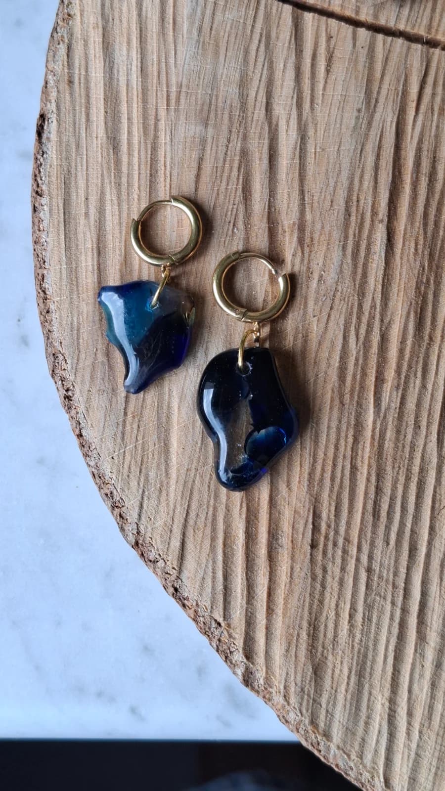 Boucles d'oreilles en verre bleu aux formes arrondies suspendues sur un fond gris clair.