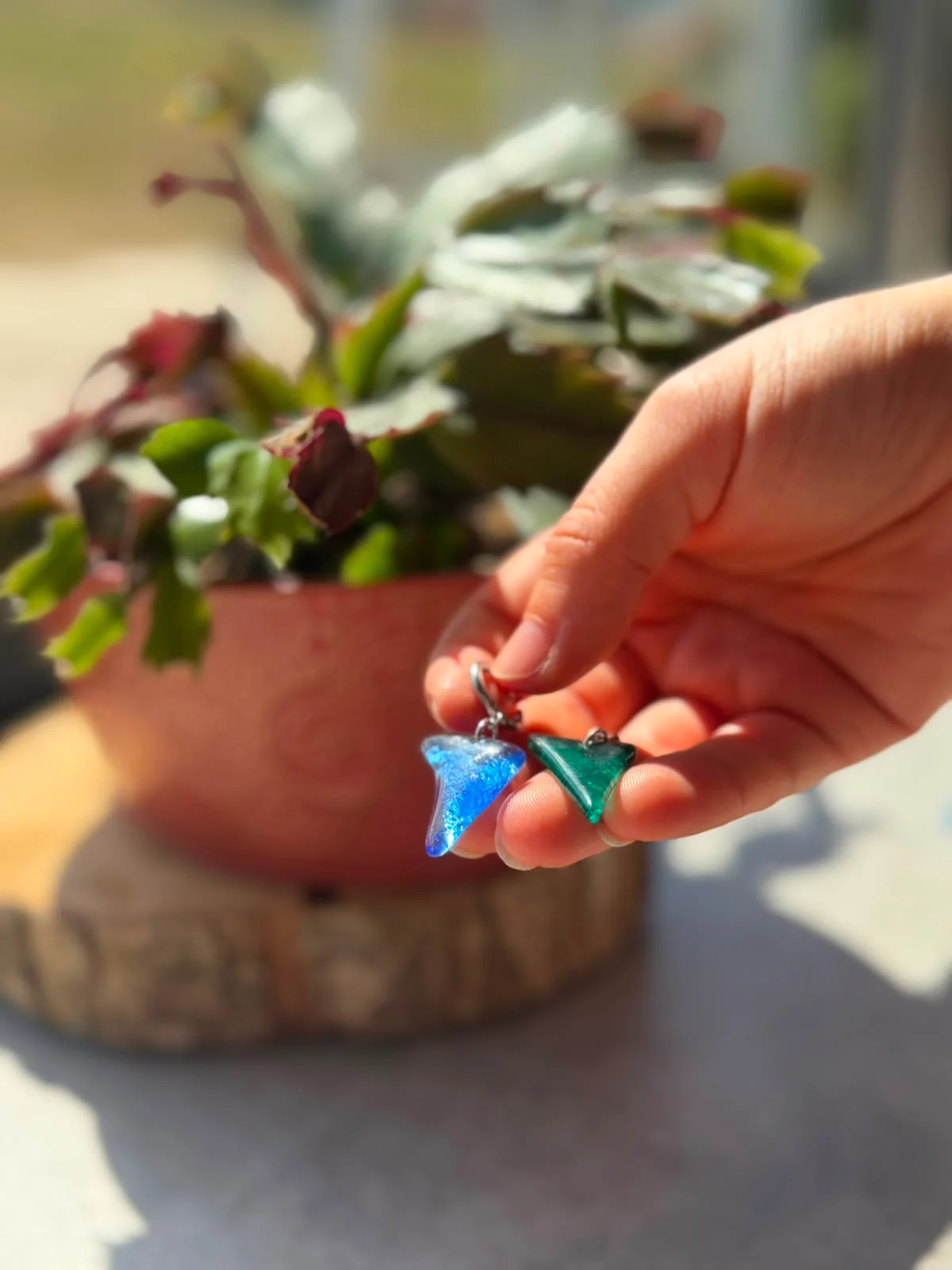 Paire de boucles d'oreilles pendantes en verre bleu et vert sur dormeuses, posées sur une rondelle de bois.