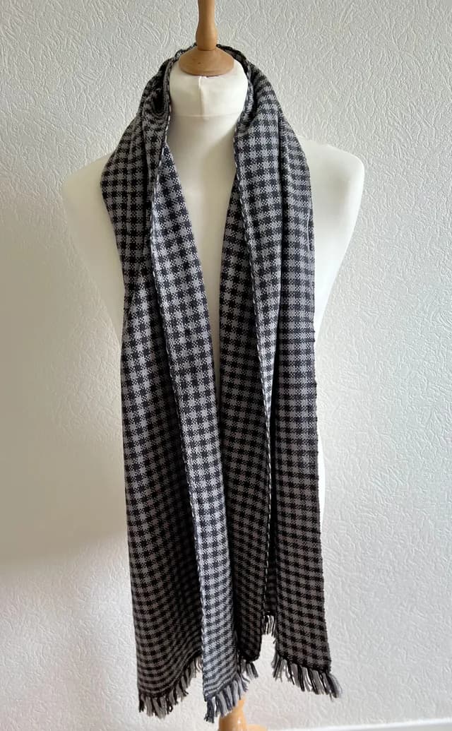 Écharpe tissée à motif quadrillé noir et blanc avec franges, portée sur un buste de mannequin blanc.