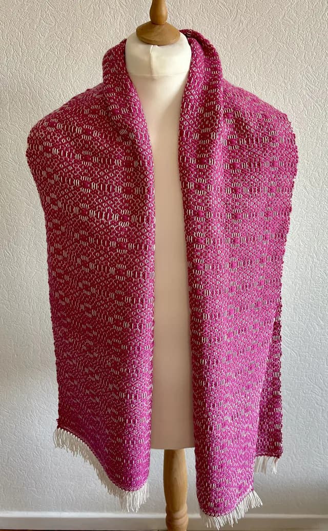 Écharpe tissée rose fuchsia et blanche à franges, portée sur un buste de mannequin.