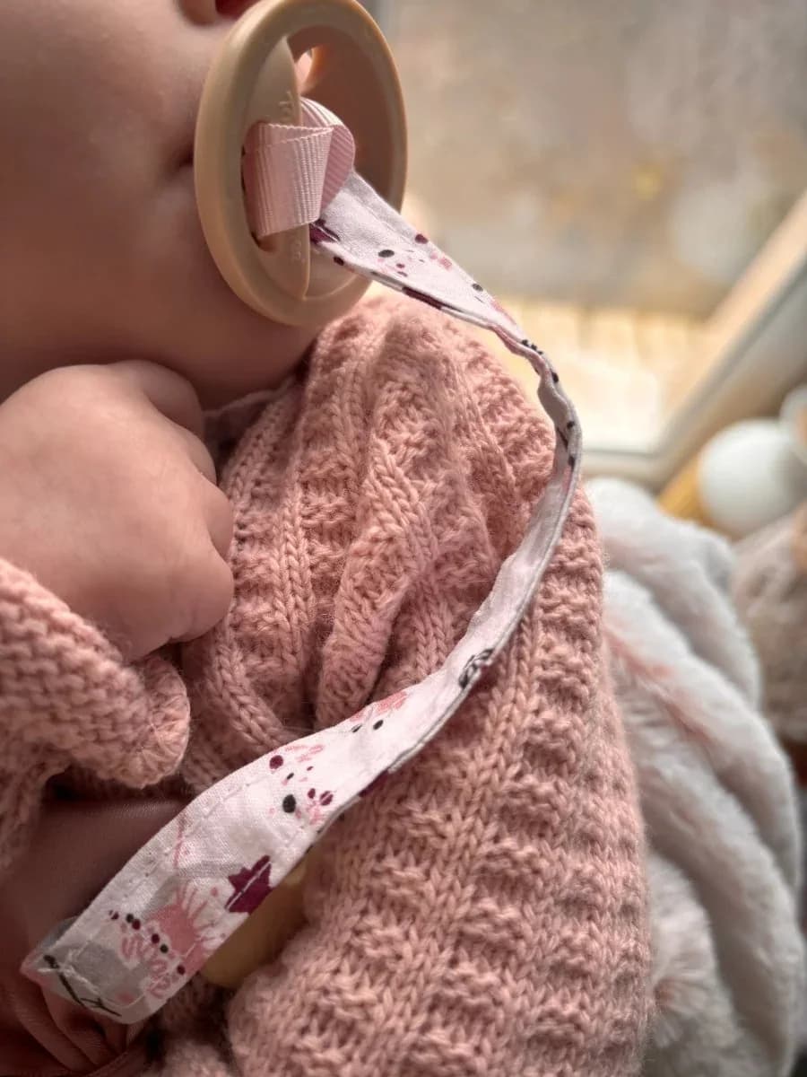 Attache-tétine en tissu à motifs roses et clip en bois clair sur fond écru texturé