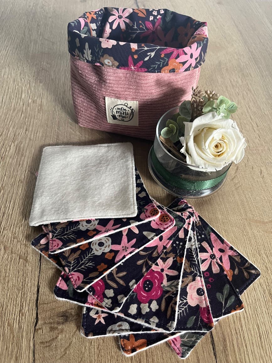 Panier rose côtelé à revers floral et lingettes lavables étalées en éventail sur une table en bois.