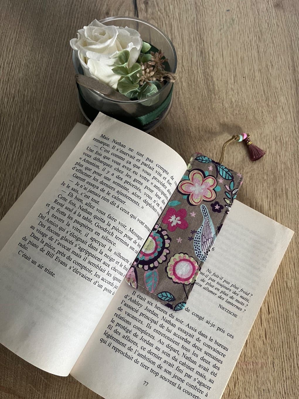 Marque-page en tissu glissé dans un livre fermé avec son pompon rose visible