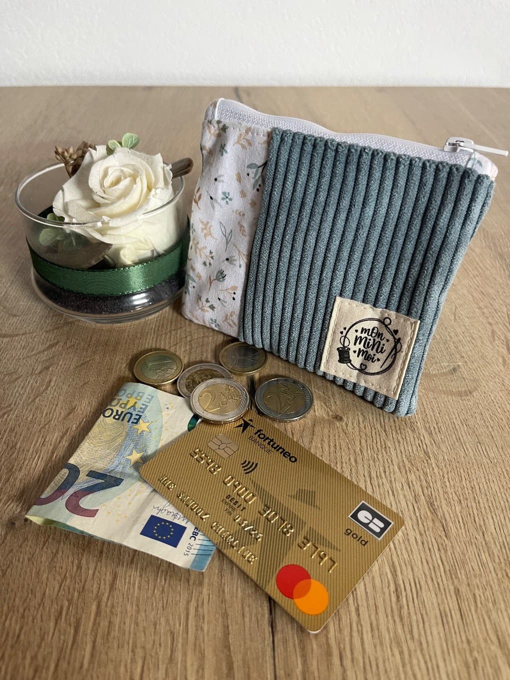 Porte-monnaie en velours côtelé bleu et tissu fleuri avec étiquette, posé avec de la monnaie.