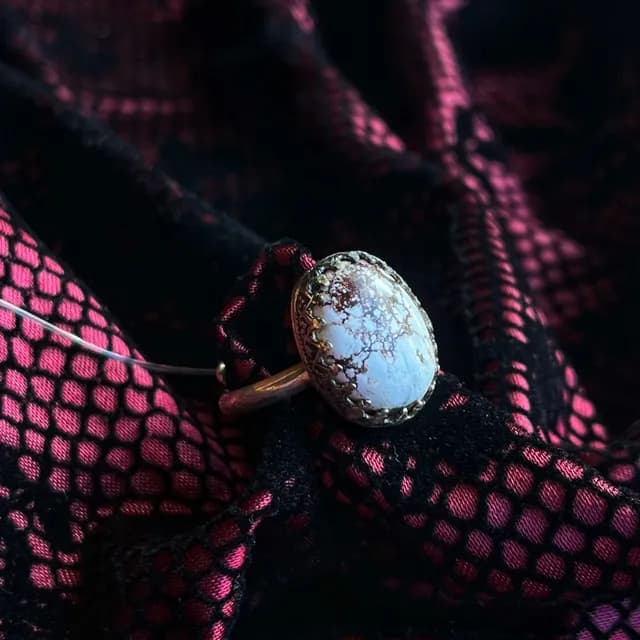 Bague avec cabochon ovale veiné et anneau argenté, posée sur un tissu ajouré noir et rose.