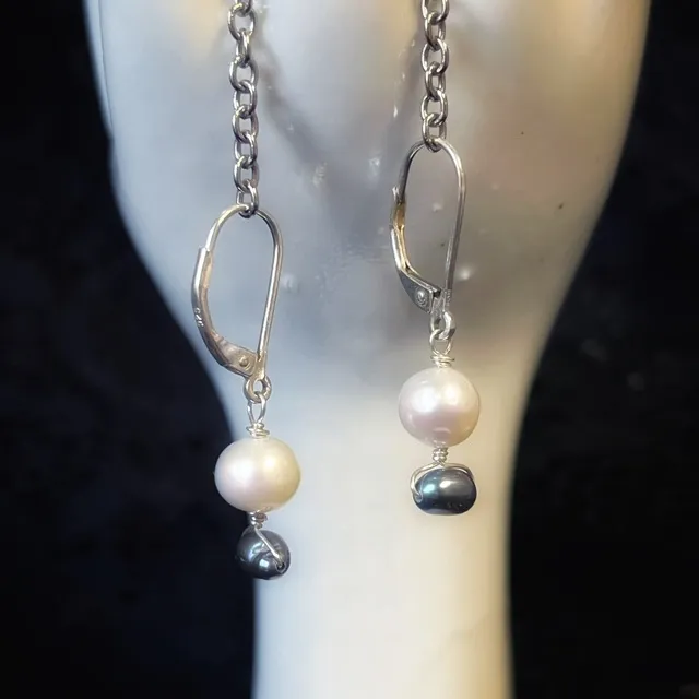 Boucles d'oreilles dormeuses à perles présentées sur une main porte-bijoux blanche sur fond de dentelle noire.