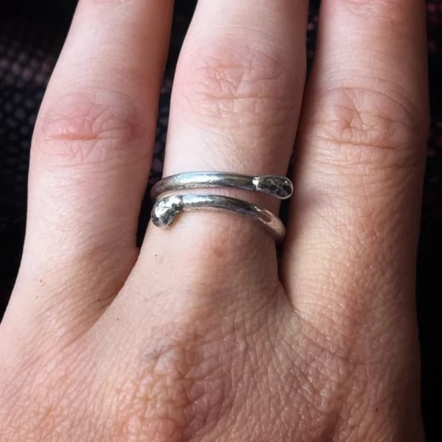 Gros plan sur une bague ajustable argentée en forme d'allumette courbée portée au doigt.