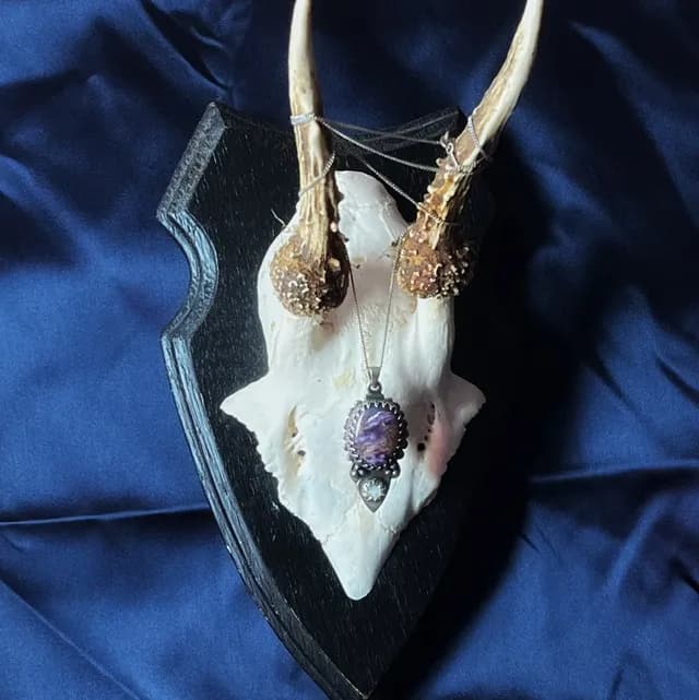 Pendentif en argent avec charoite violette et opale, suspendu à un trophée crânien sur tissu bleu.