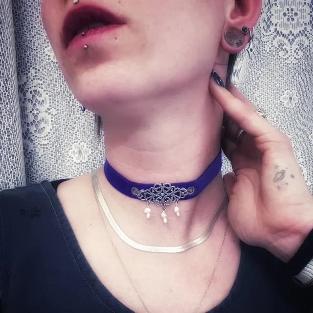 Collier ras de cou en velours violet orné d'un médaillon en métal ajouré et de perles, porté.
