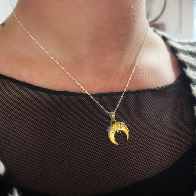 Pendentif lune dorée et argentée porté au cou sur une fine chaîne torsadée.