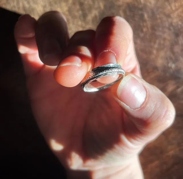 Bague argentée martelée tenue entre les doigts, mettant en valeur son anneau mobile gravé.
