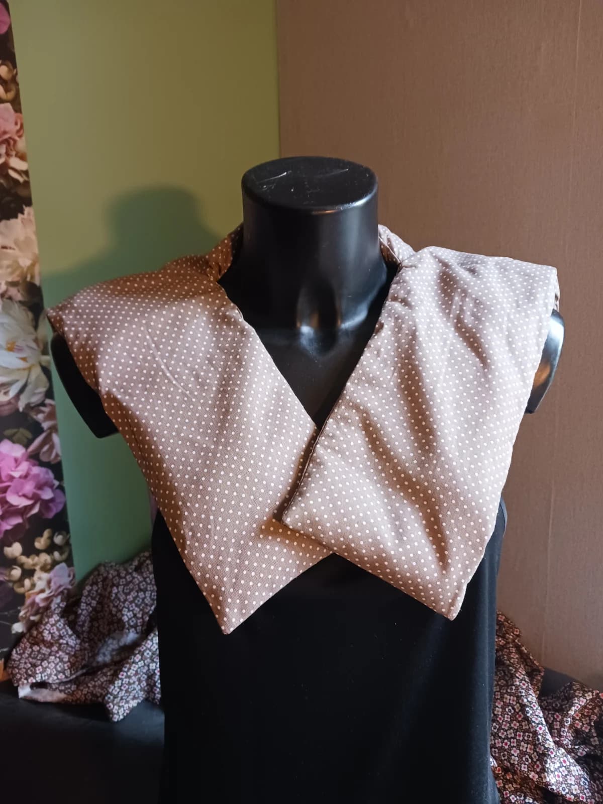 Bouillotte beige taupe à pois blancs posée sur les épaules d'un mannequin noir, vue de face.