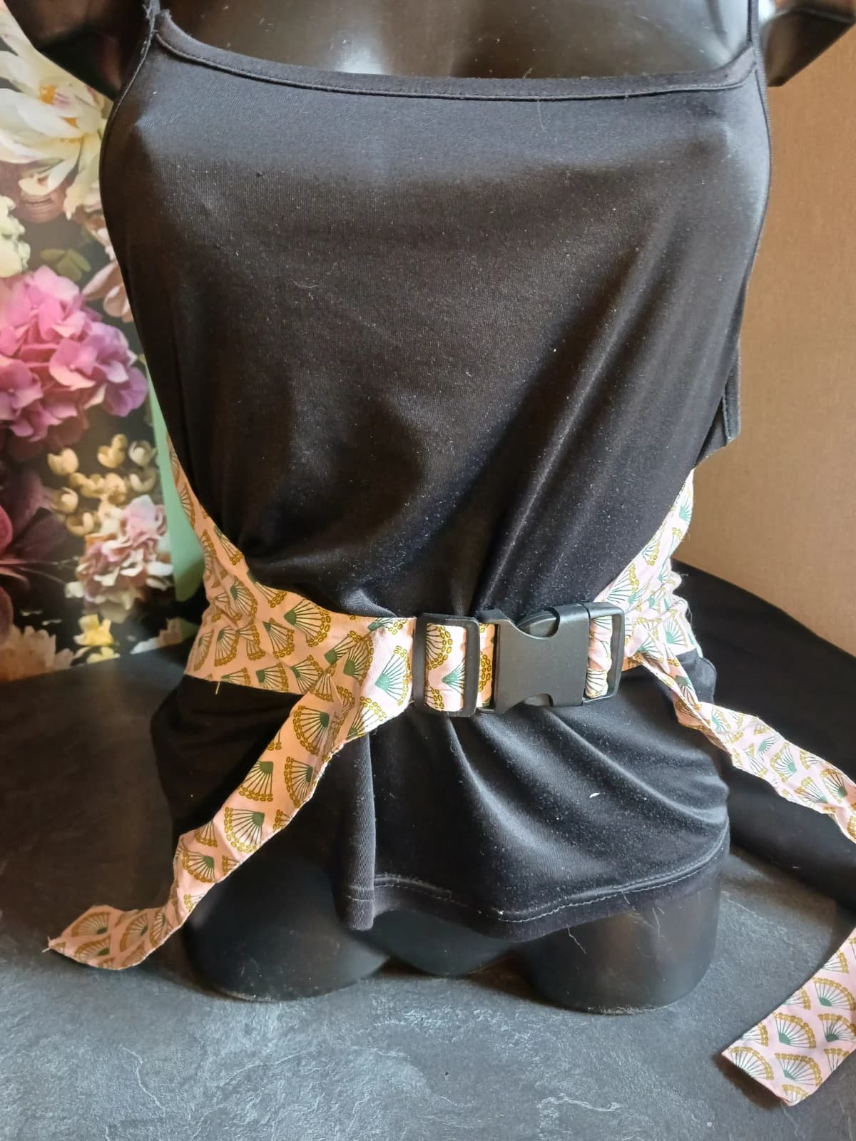 Ceinture bouillotte attachée sur buste avec boucle en plastique noir et lanières à motifs éventails rose et vert.
