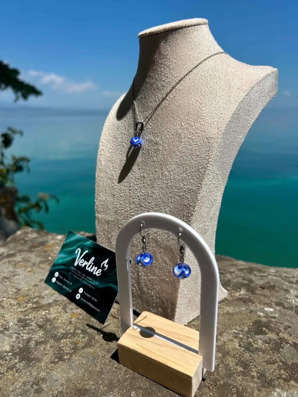 Collier et boucles d'oreilles aux perles bleues et blanches présentés sur présentoirs en extérieur face à l'eau.