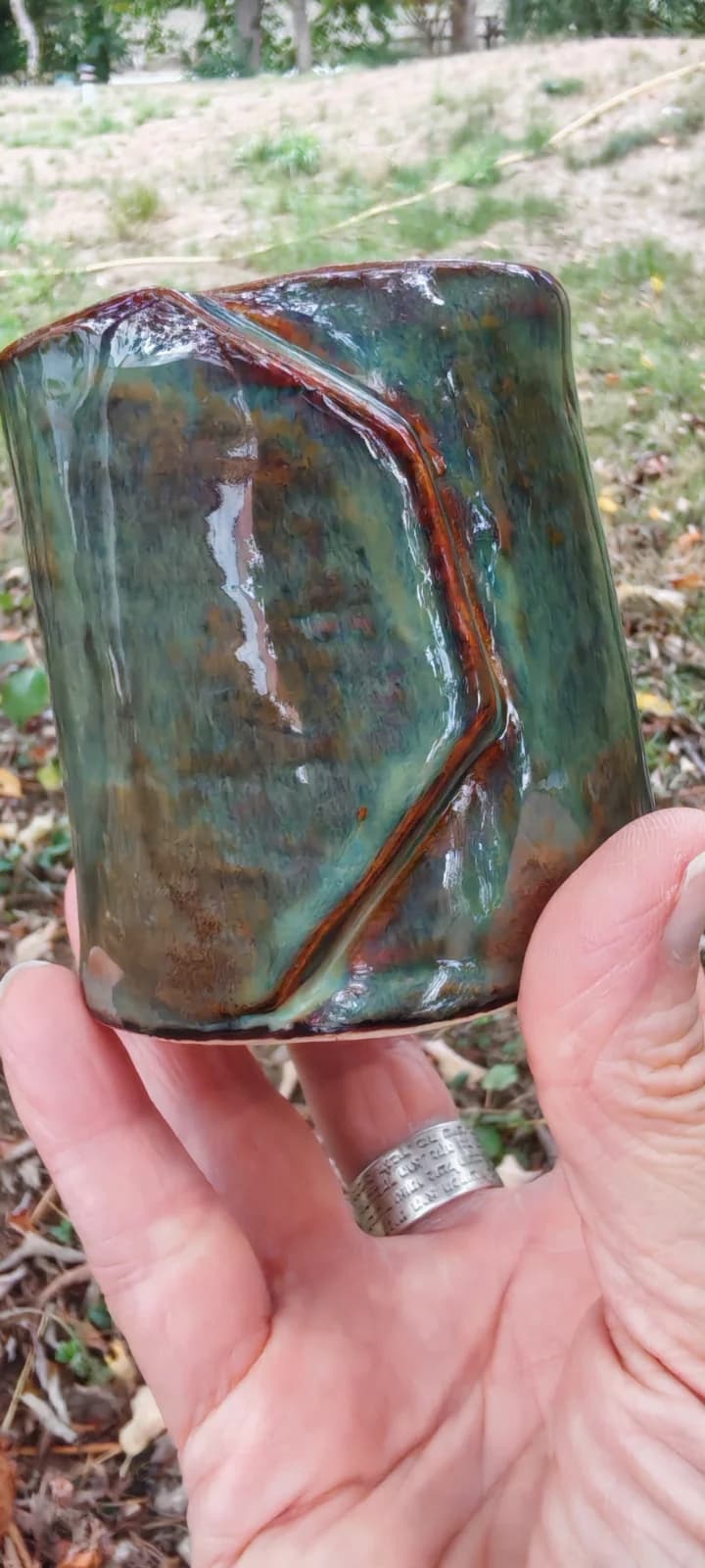 Gobelet artisanal émaillé aux teintes vertes et brunes tenu dans la main