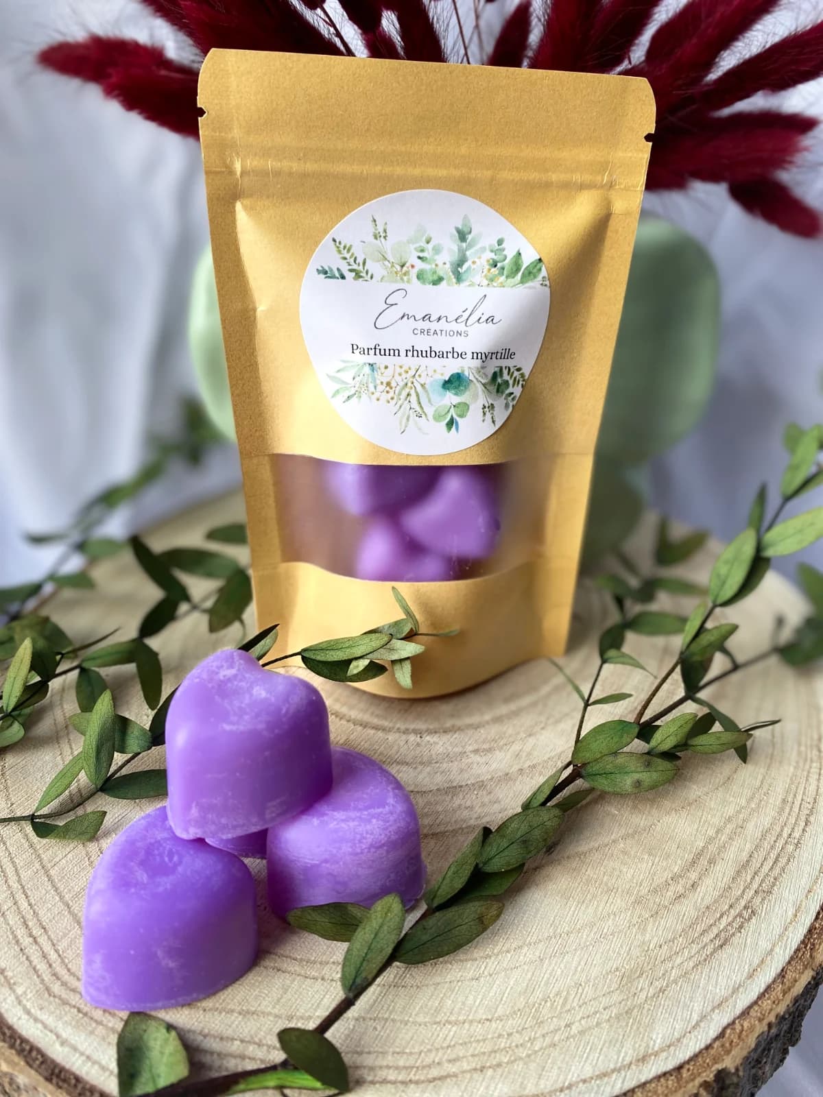Sachet kraft et fondants violets en forme de cœur présentés sur une rondelle de bois avec végétaux.