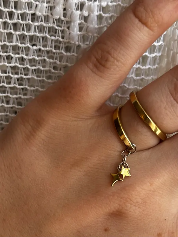 Bague double anneau dorée portée au doigt, avec breloque à deux étoiles suspendues